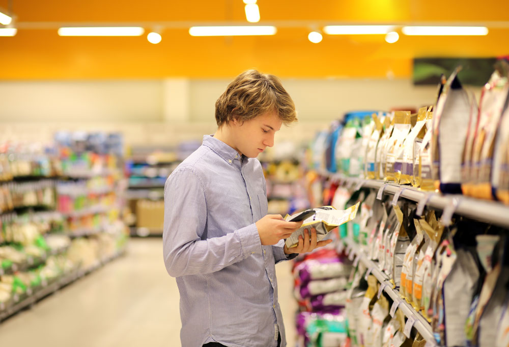 young consumer looking at phone standing in grocery store